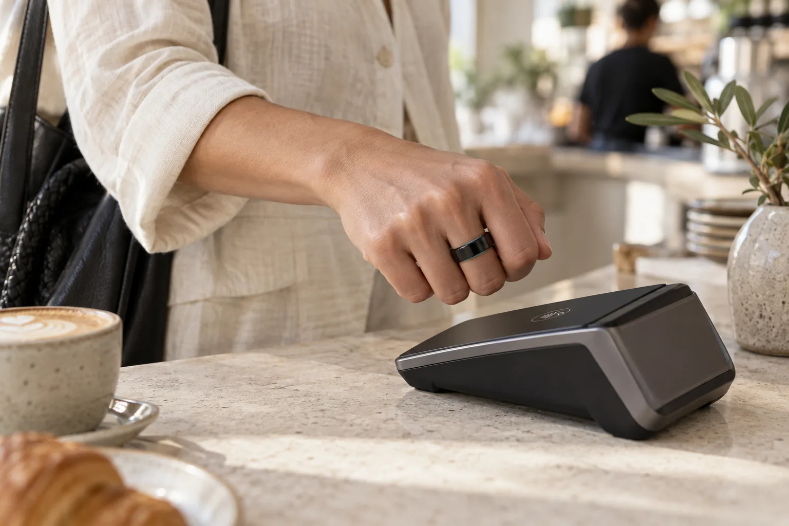 A customer tapping a slim black NFC ring at a café payment terminal